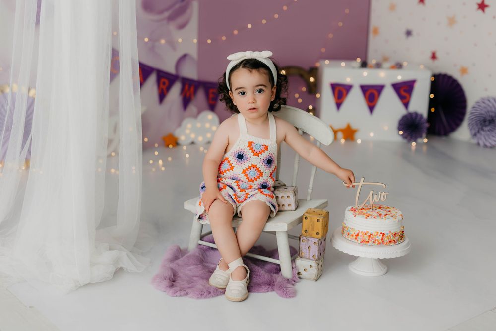 Fotografía del segundo año de una niña con tarta y con decoración en tonos morados.