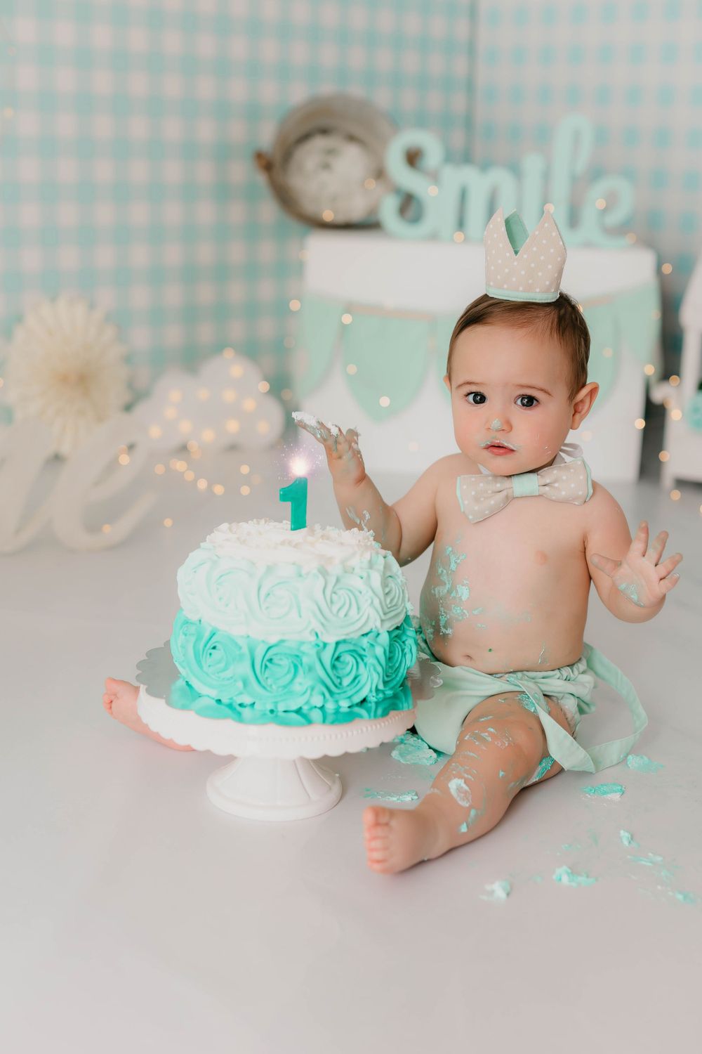 Foto del primer añito de un niño con tarta y peto en tonos mint y beige en su sesión en estudio.