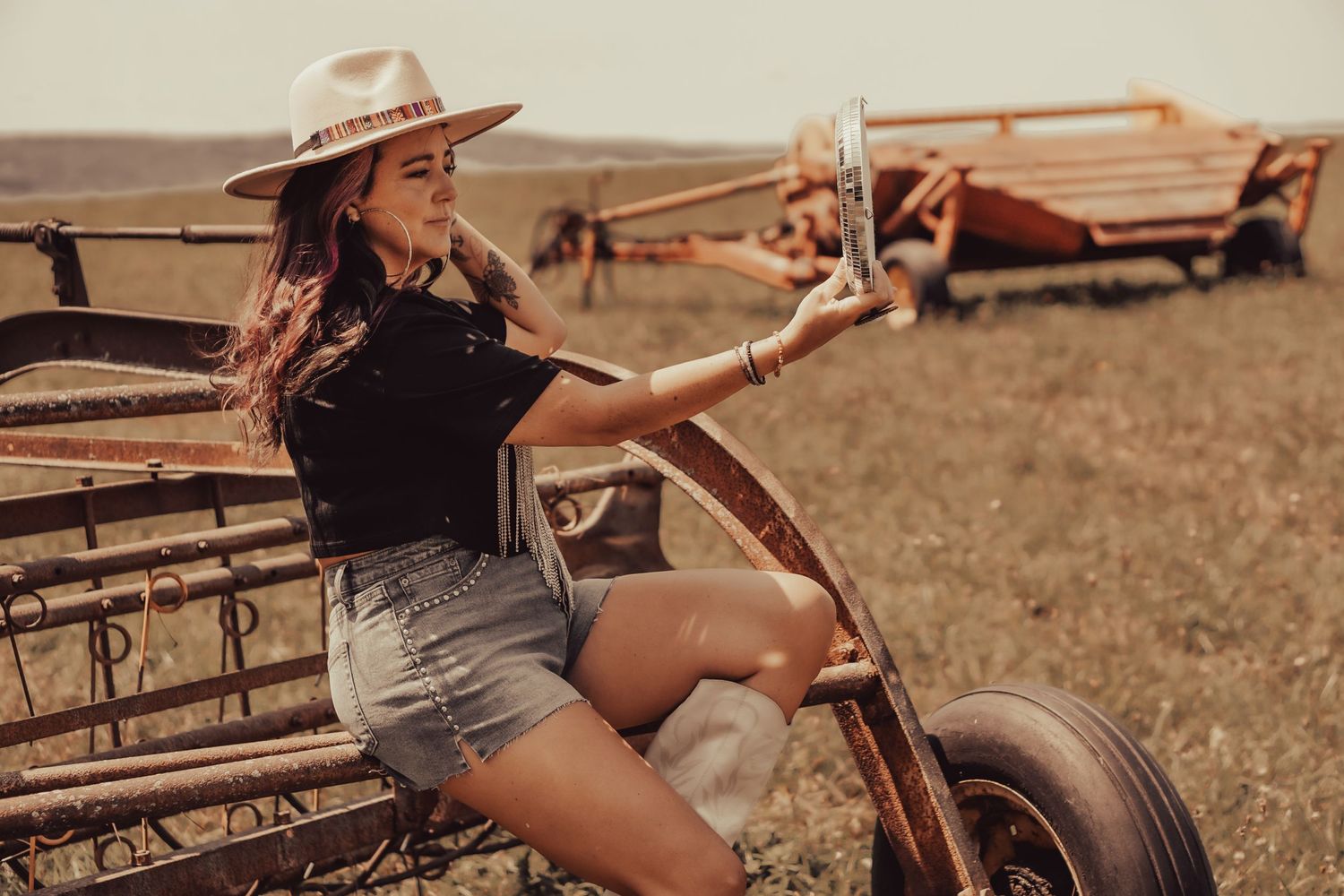Vintage-style photo of woman in hat posing on rustic farm equipment.