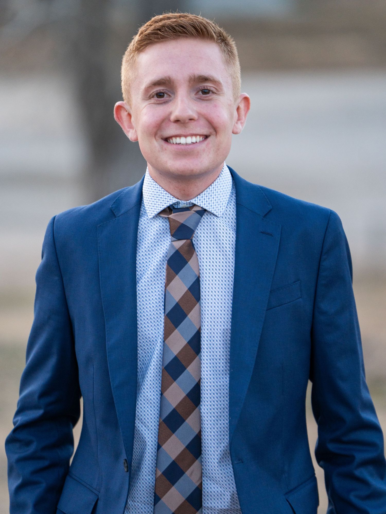 Professional portrait of person in navy suit with striped tie and light blue shirt.