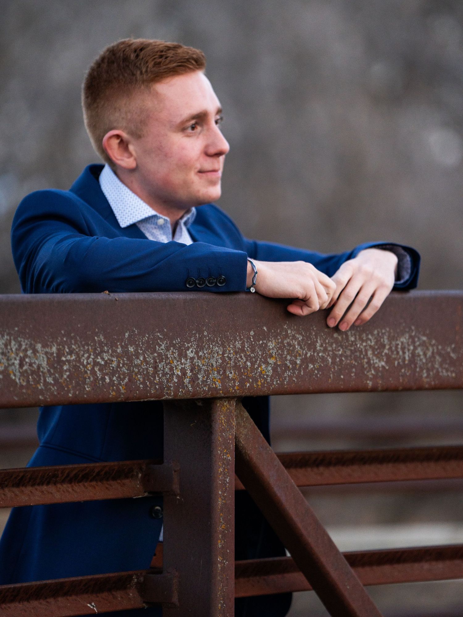 Casual portrait of person leaning on rustic metal railing wearing navy suit.