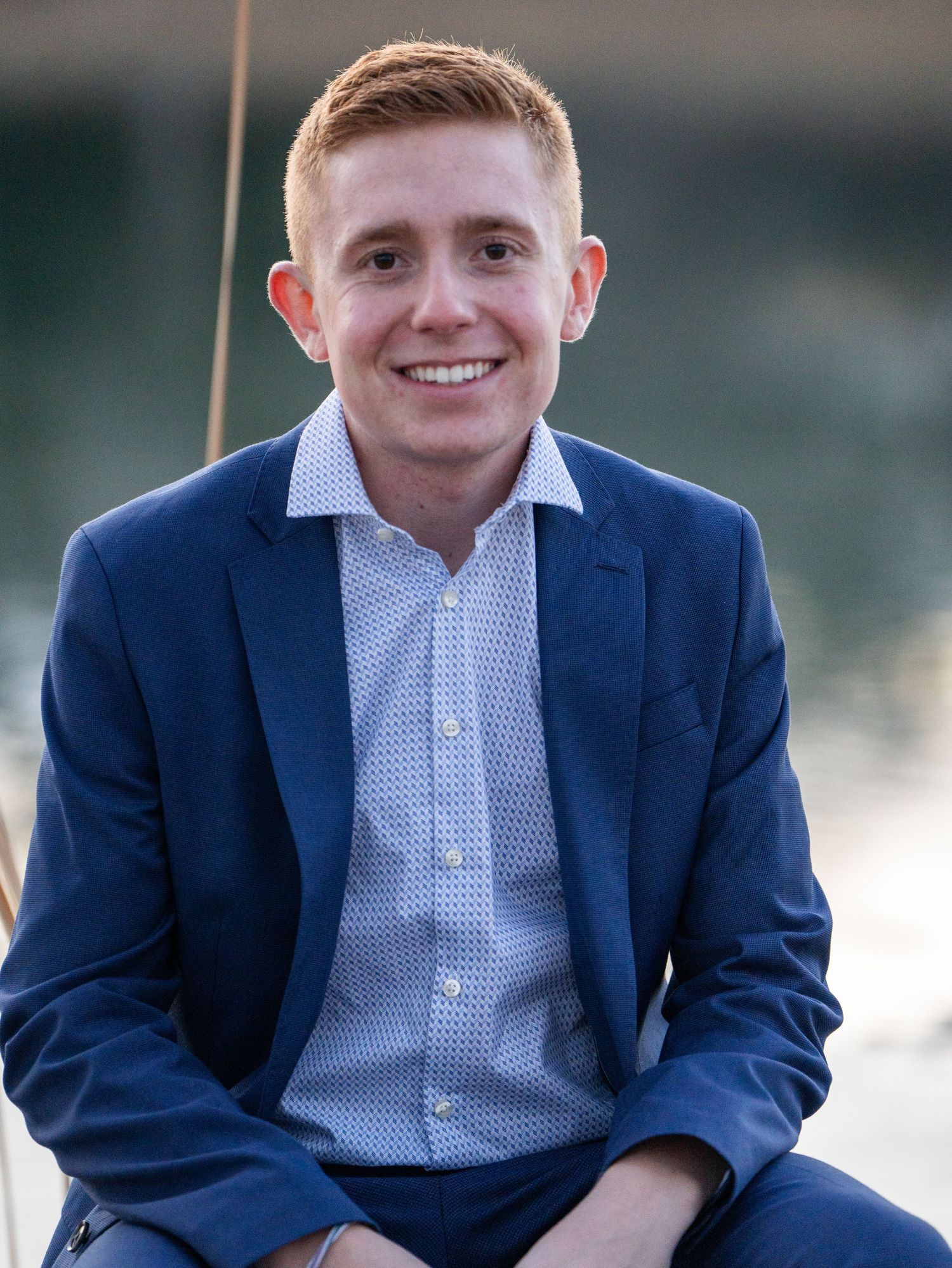 Professional headshot portrait of person in navy suit with patterned dress shirt.