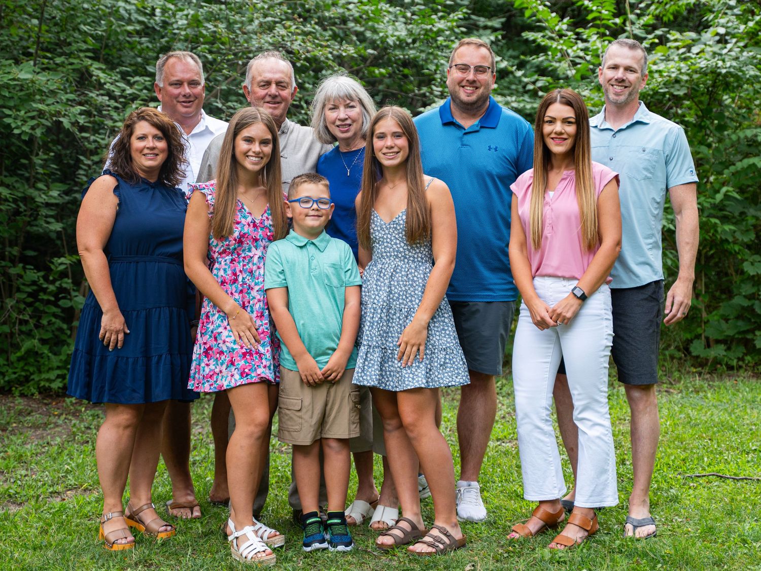 Multi-generational family group photo outdoors wearing coordinated blue and white summer outfits.