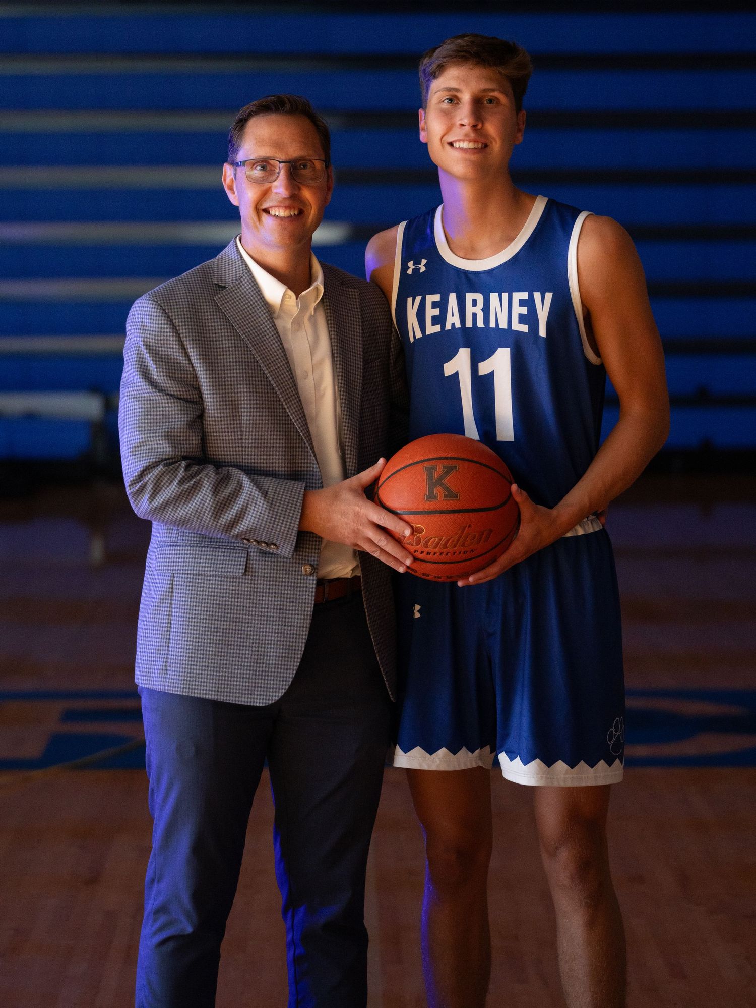 A father and son pose together holding a ball in a gymnasium.