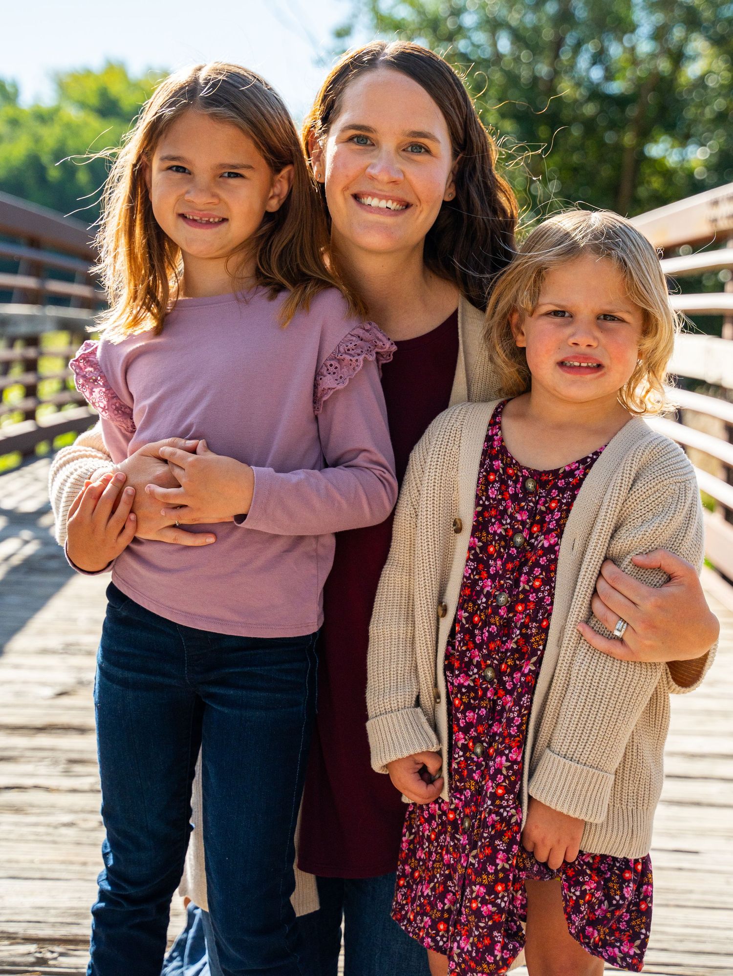 A family in coordinated outfits poses together on a wooden bridge during a sunny day.