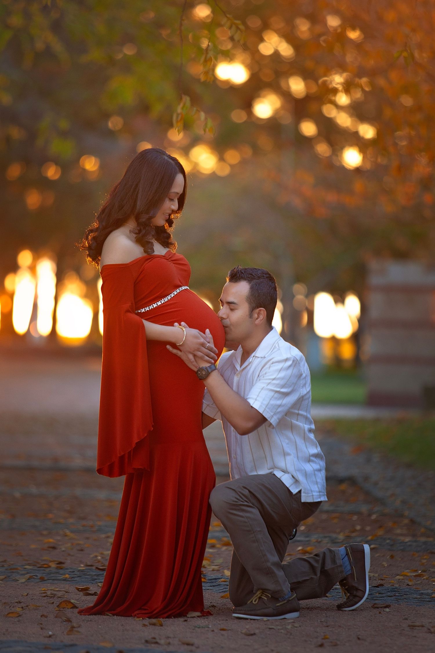 Couple sharing a tender maternity moment in a park, man kissing pregnant belly at sunset.