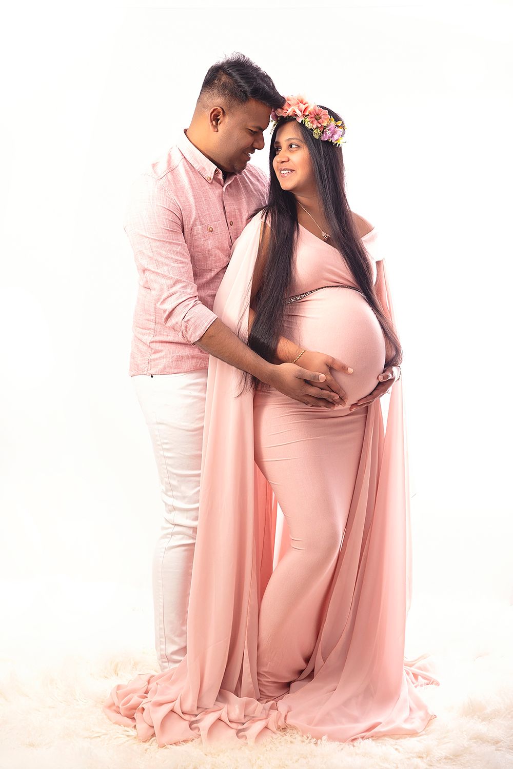 Expecting couple in matching pink outfits sharing a tender moment during a maternity photo session.