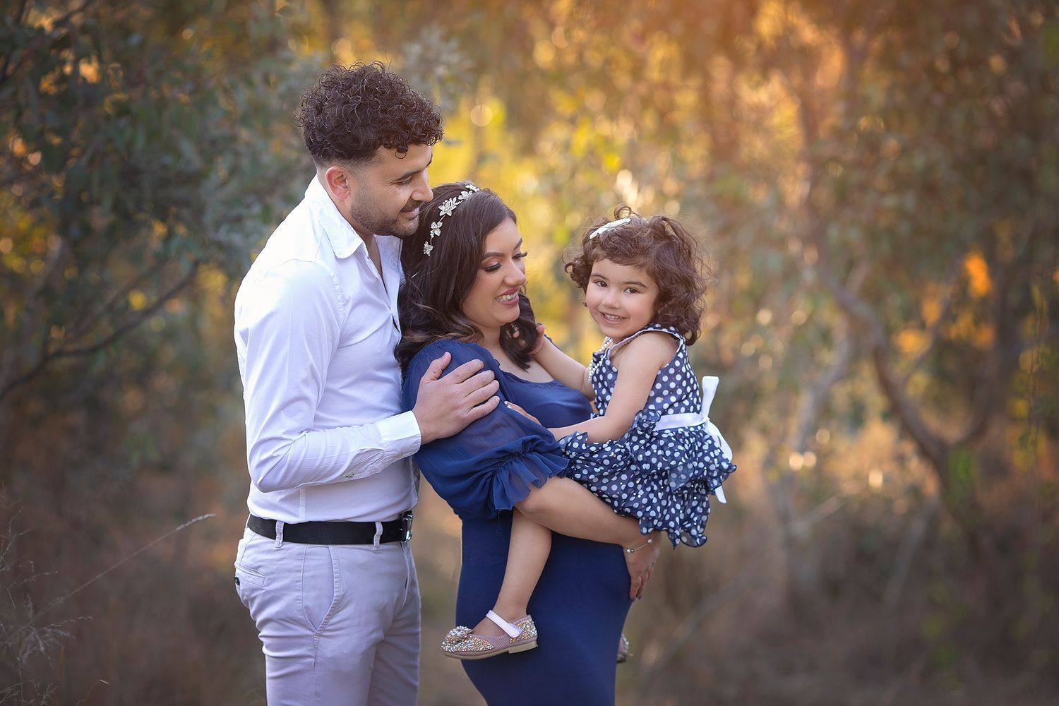 Happy family of three embraces in golden autumn outdoor setting, mother holds young daughter.