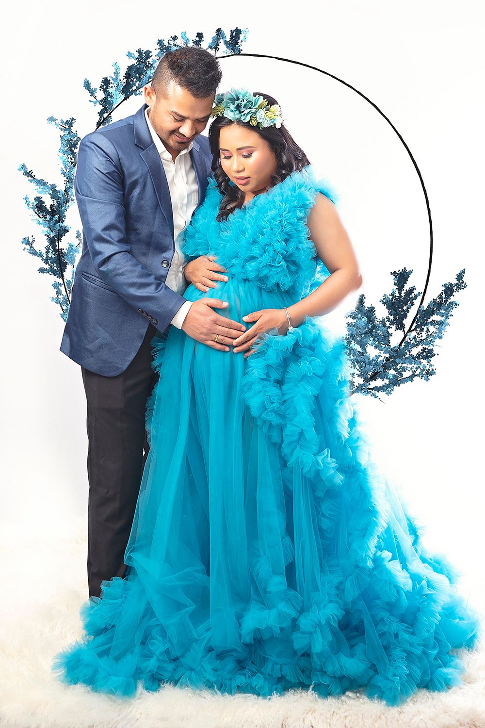 Couple in blue maternity photoshoot with tulle gown and floral arch.