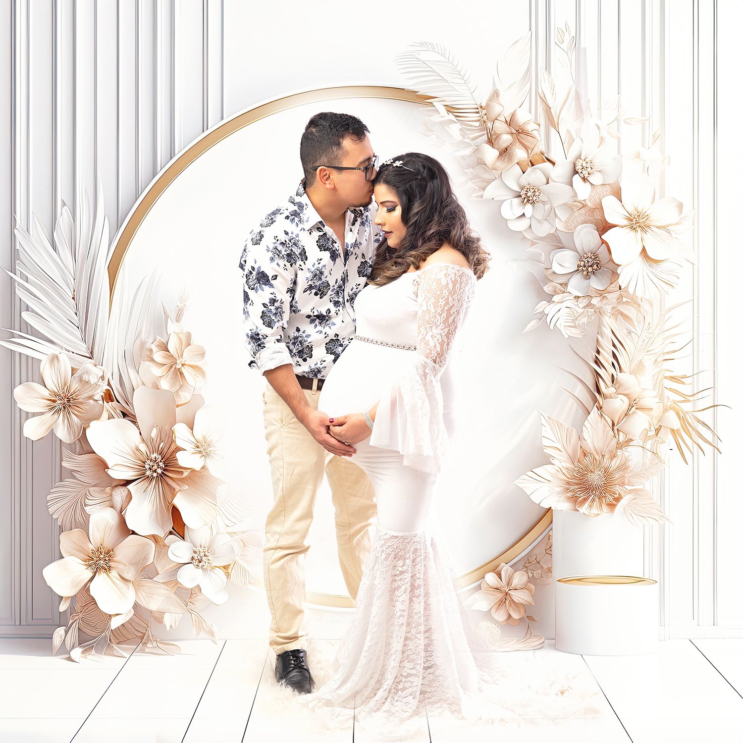 Couple shares a kiss in boho maternity photo with white floral arch and golden ring backdrop.