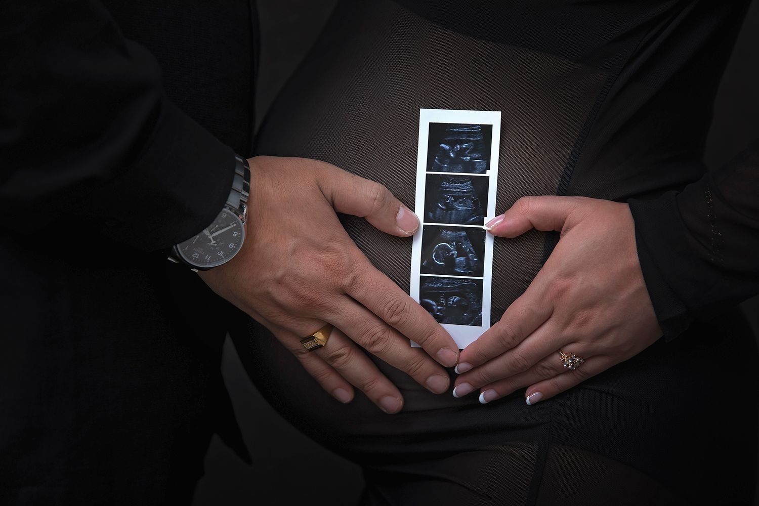 Close-up of couple holding ultrasound photos against pregnant belly during maternity photoshoot.