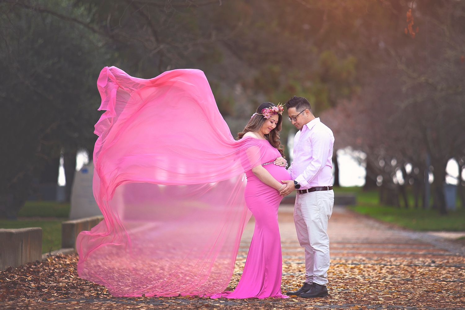Expecting couple sharing tender moment, woman in pink flowing maternity dress in autumn park.