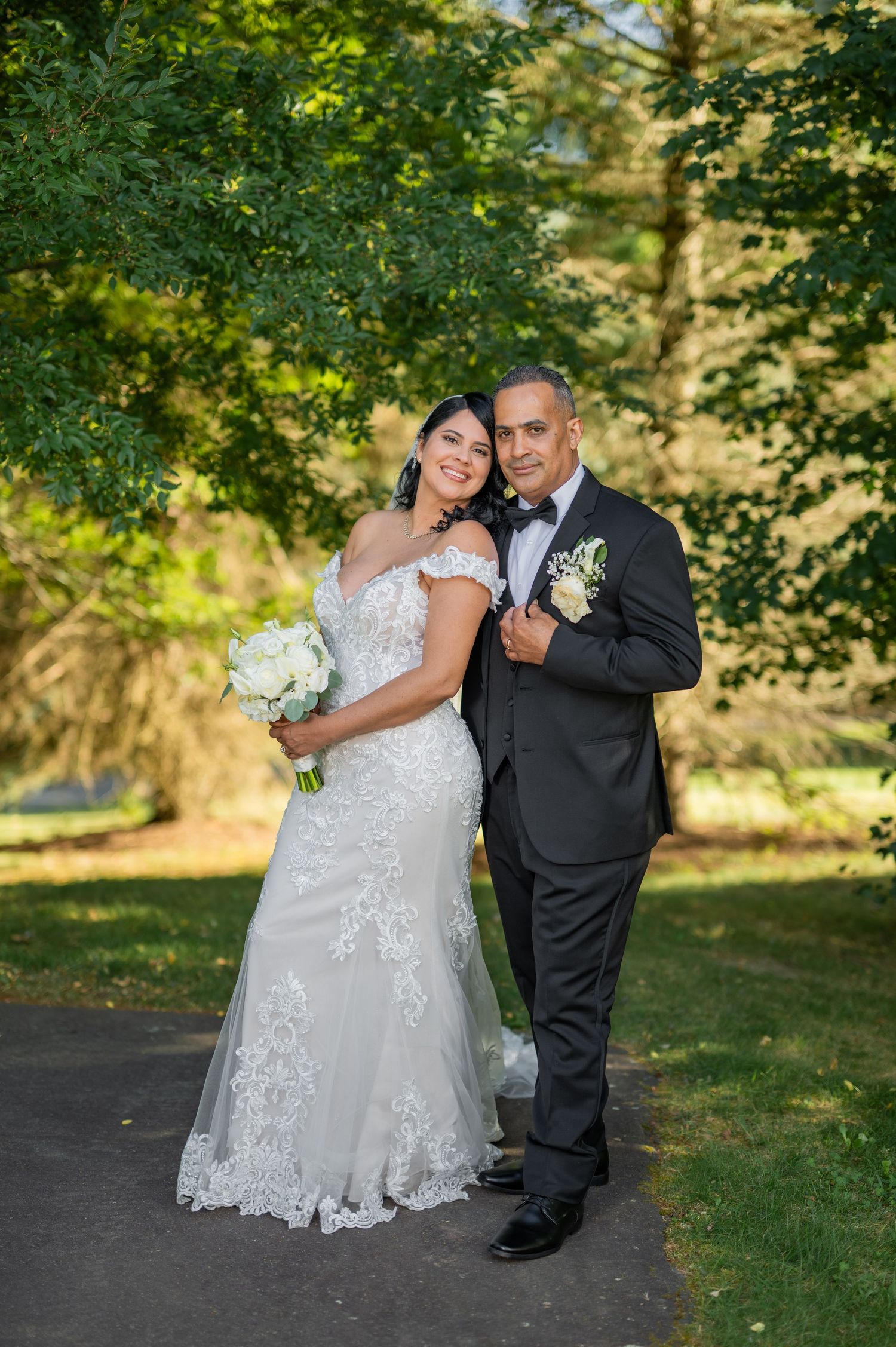Wedding couple poses in front of stone church with beautiful floral bouquet and bridal veil.