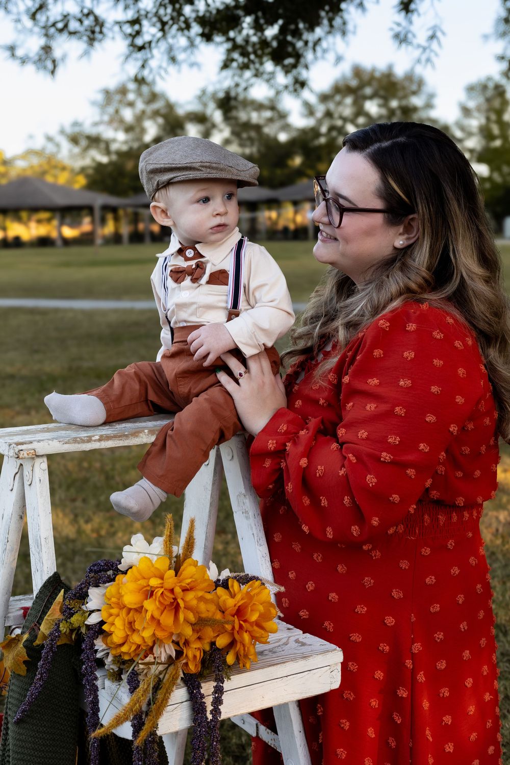Outdoor fall portrait with red polka dot dress and white ladder decorated with yellow flowers.