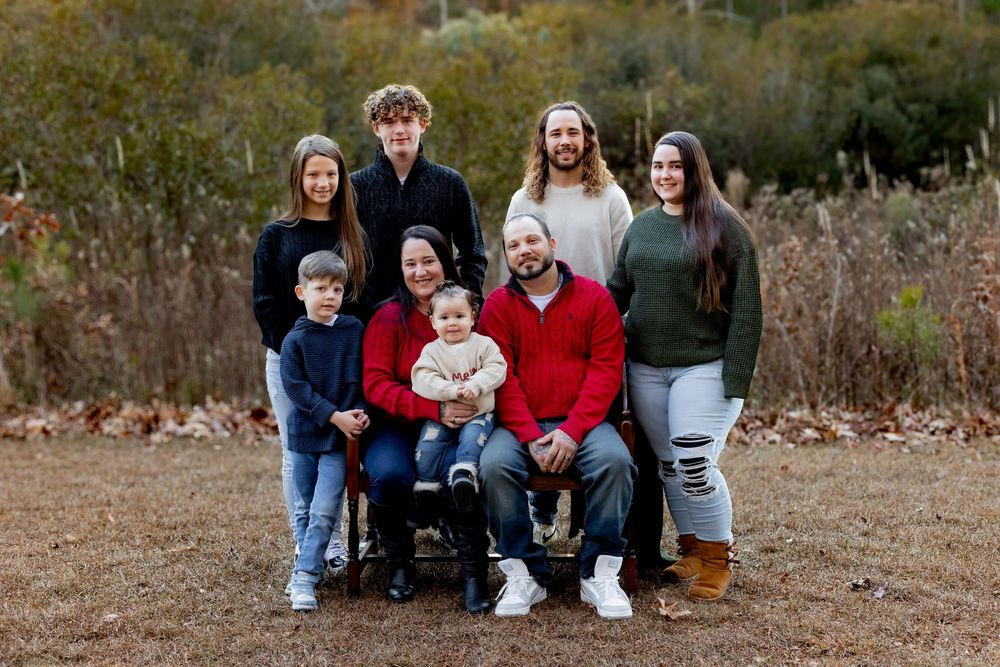 A family sits together outdoors on fallen autumn leaves for a casual photo session.