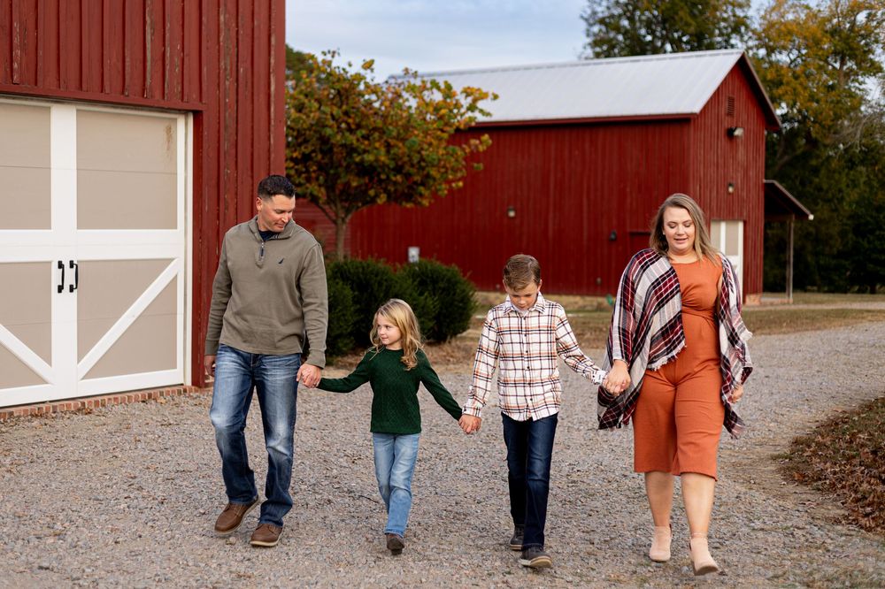 A group walks hand in hand down a gravel path in front of a red barn on an autumn day.