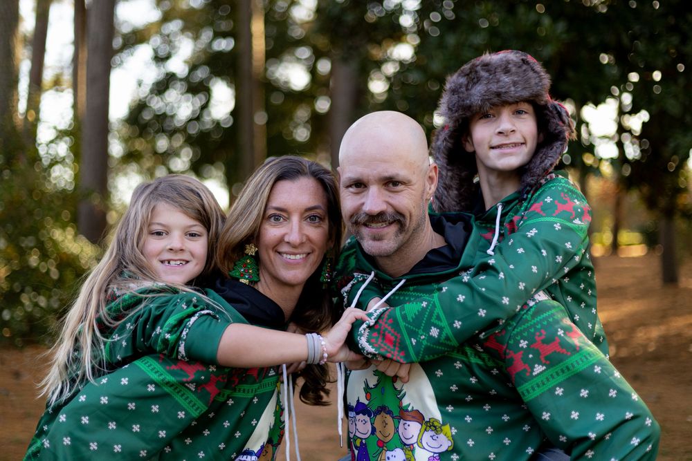 Family group wearing coordinated green and white polka dot outfits poses together outdoors in a wooded setting.