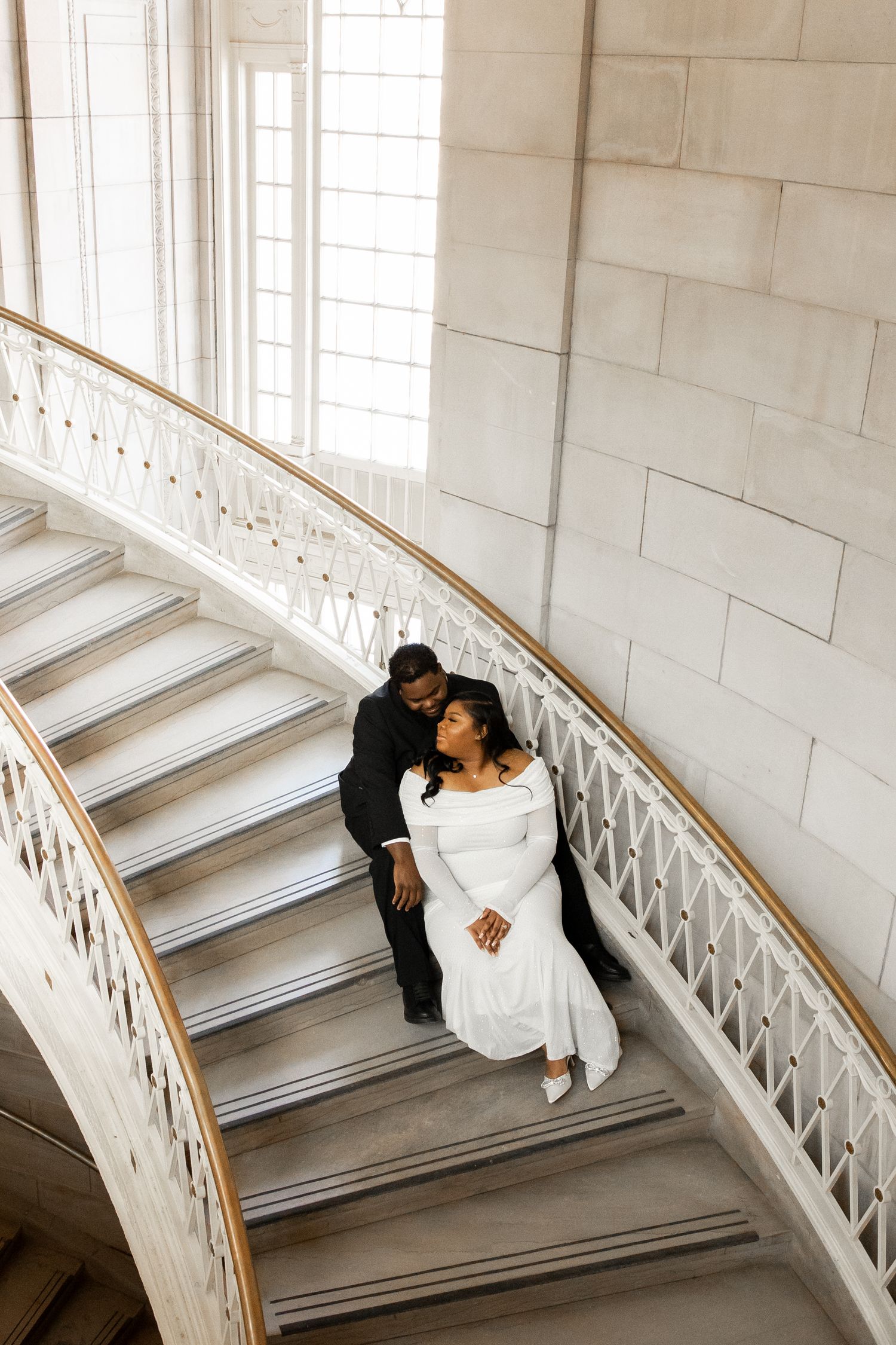 Elegant couple in formal attire seated on grand marble staircase.