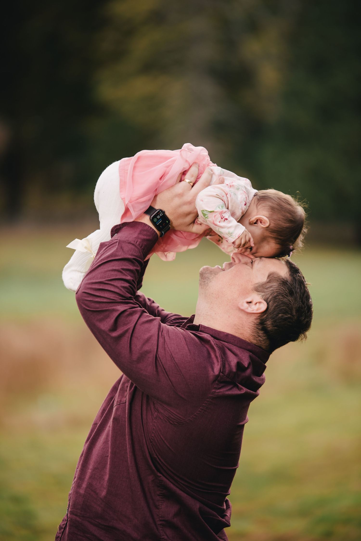 Parent lifting baby high in the air on an autumn afternoon in the park.