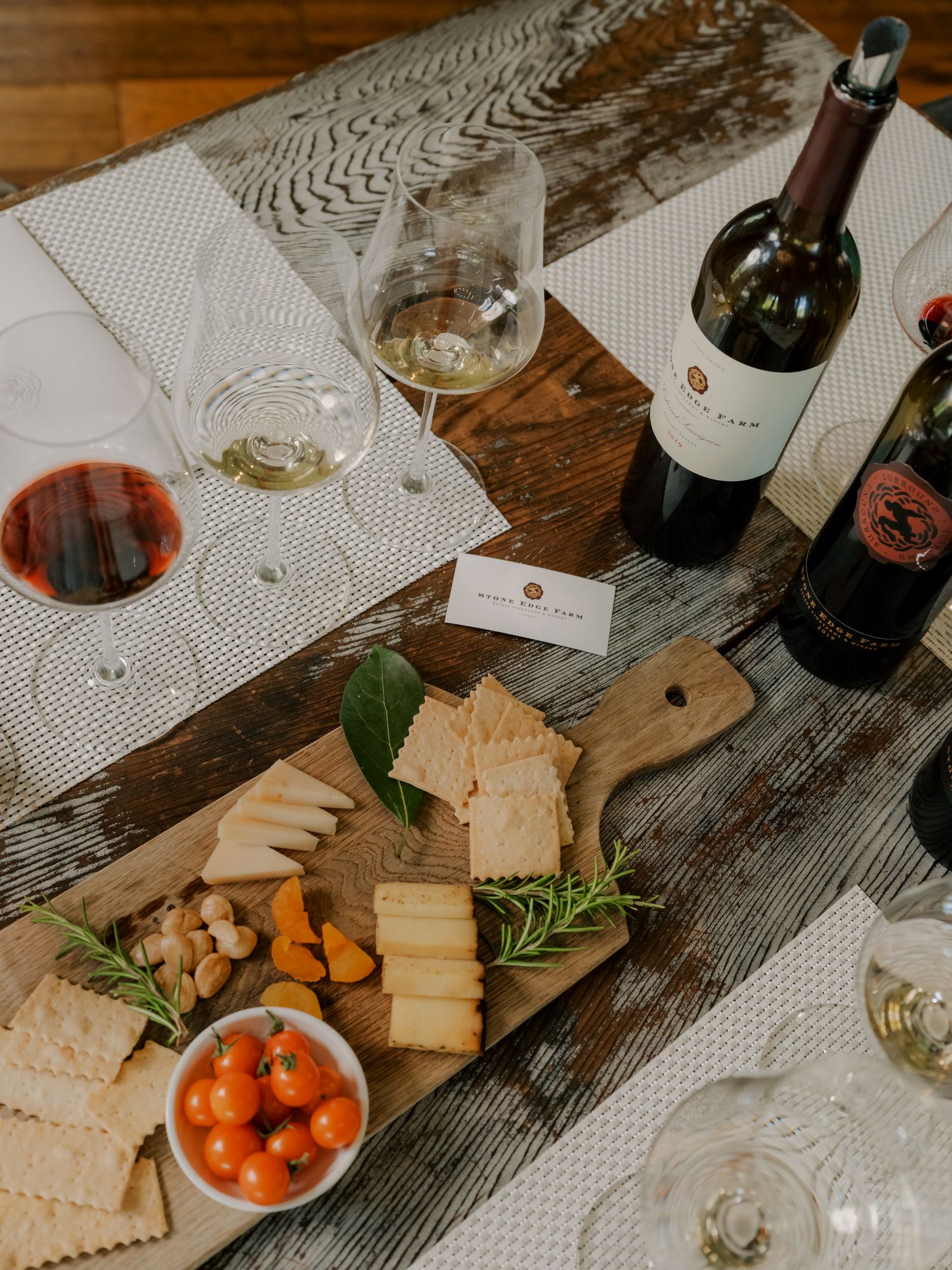 Wine tasting setup with cheese board, cherry tomatoes, crackers and glasses on rustic wooden table.