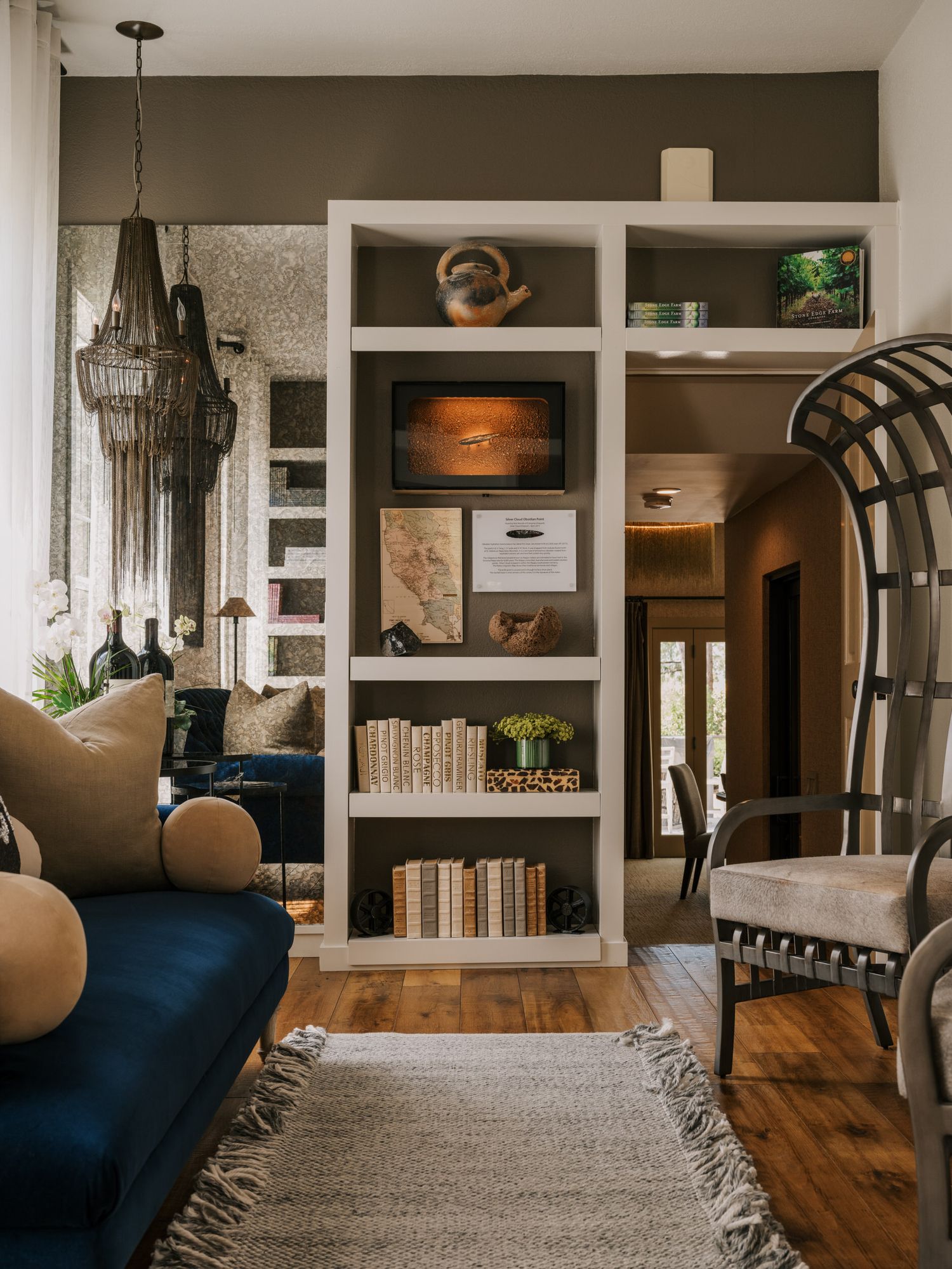 Modern living room featuring blue velvet couch, built-in white shelving, chandelier, and arched doorway with hardwood floors.
