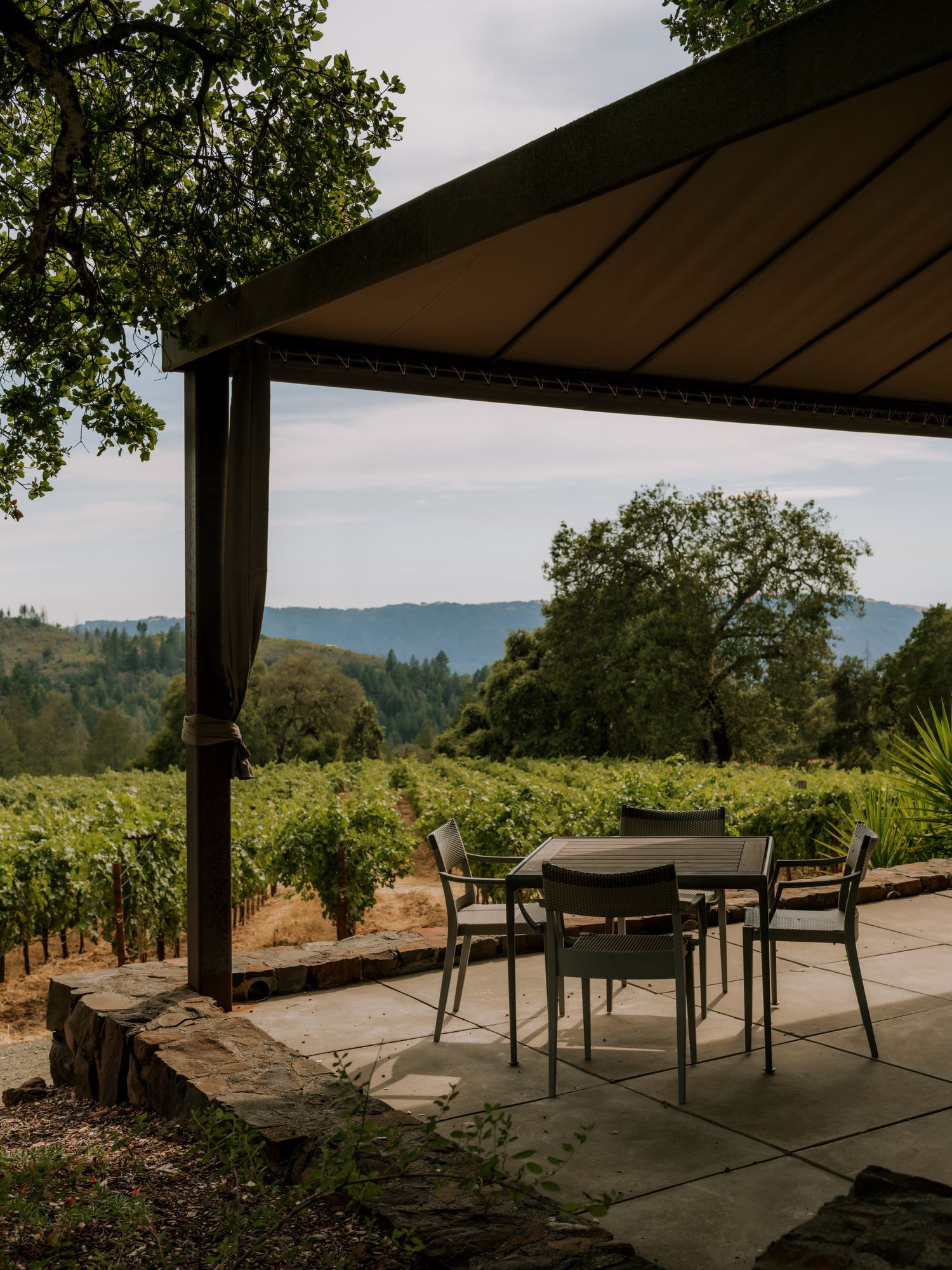 Covered patio with outdoor furniture overlooking scenic vineyard and rolling hills in wine country.