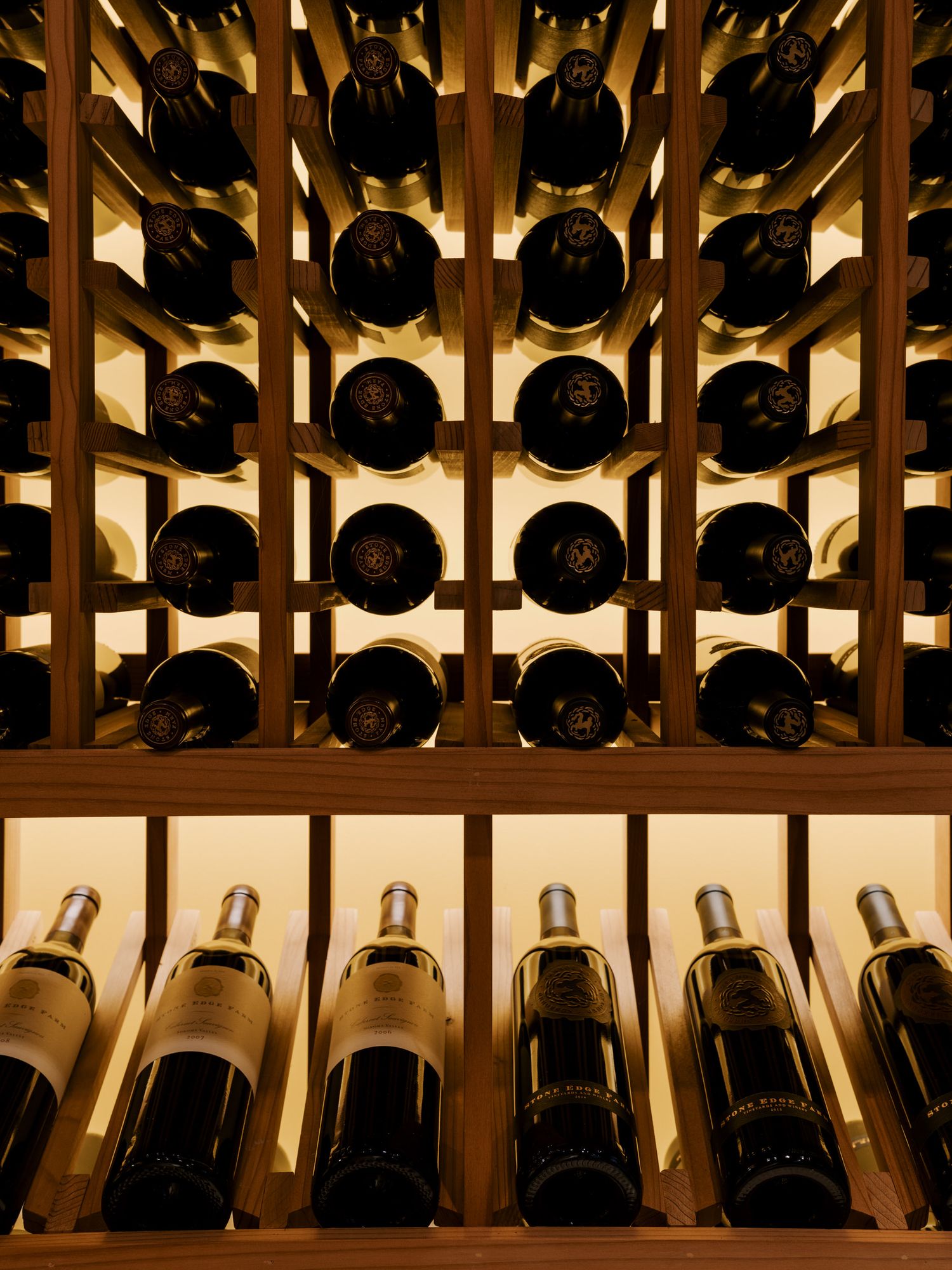Wooden wine rack displays dark bottles arranged in rows with warm lighting illuminating the collection.