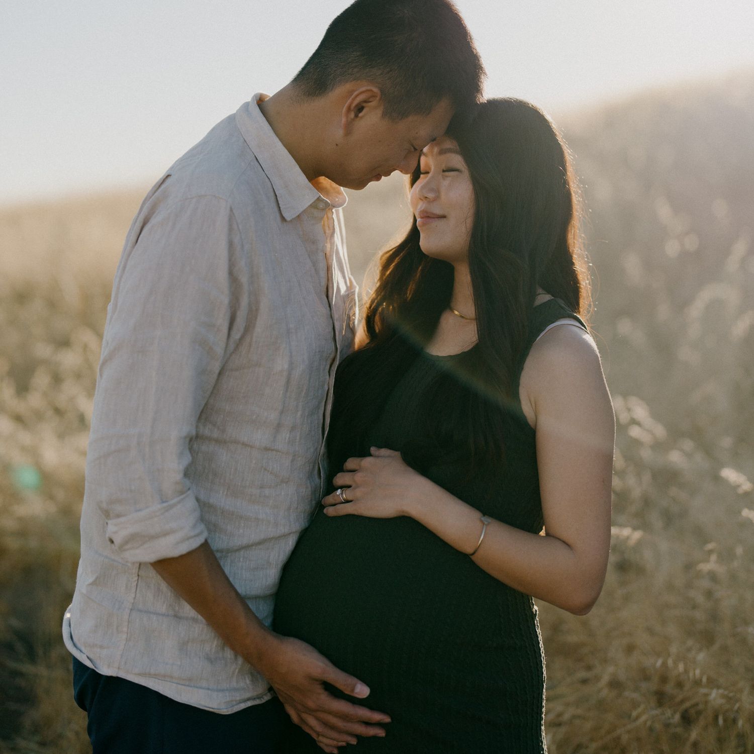 An intimate maternity portrait captured in warm evening light among golden grasses.