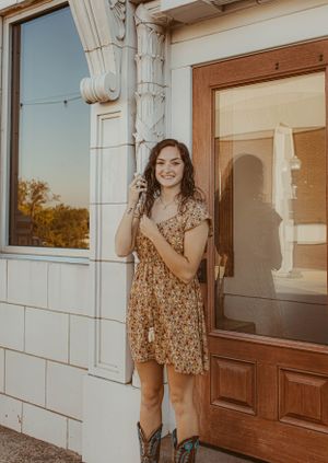 Person in floral dress and cowboy boots standing by vintage doorway at sunset.