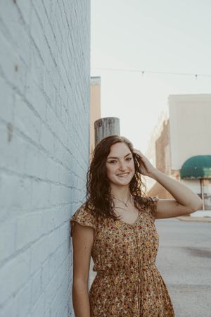 Portrait against white wall in floral dress during golden hour.