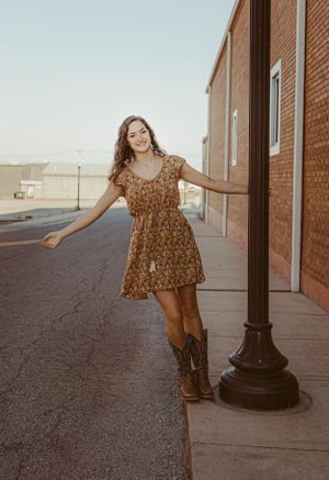 Person in floral dress and boots posing by vintage lamppost on urban street.