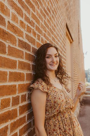 Portrait against brick wall wearing floral dress in warm sunset light.