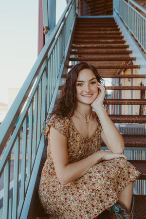 Portrait on metal staircase wearing floral dress at sunset.
