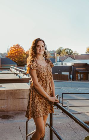 A floral dress and curly hair create an autumn rooftop portrait with golden sunlight and city buildings in the background.