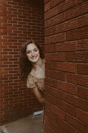 Playful portrait peek around a brick corner wearing a floral dress.