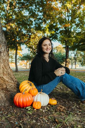 Autumn scene with decorative pumpkins and casual fall fashion by a large tree.