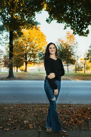 Casual autumn portrait with black sweater and jeans against fall foliage background.