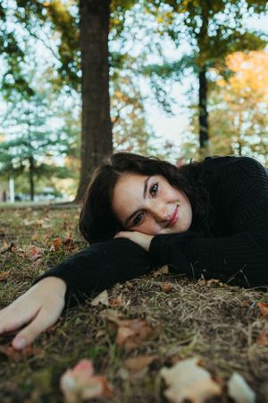 Relaxed outdoor portrait lying on fallen leaves wearing a black sweater.
