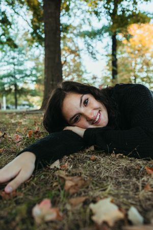 Lying on autumn leaves wearing a cozy black sweater during a fall photoshoot.