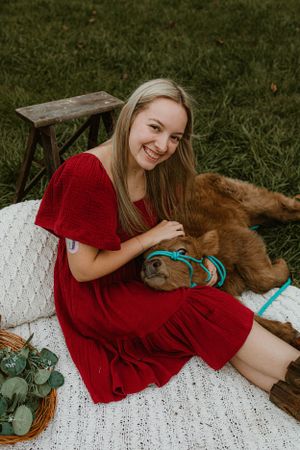 Woman in red dress sitting with baby calf on white blanket outdoors.