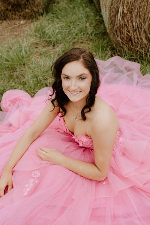 A portrait of someone in a pink princess ball gown sitting near hay bales outdoors.