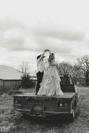 A couple dancing on the back of a rustic flatbed truck in formal attire.