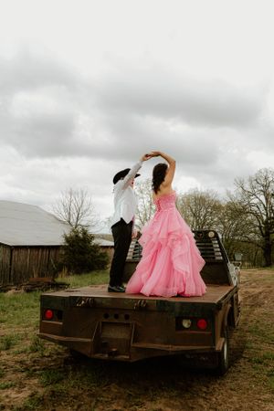 A couple in formal wear dancing on a flatbed truck with a barn in background.