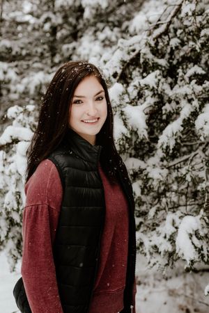 Winter portrait of person in red sweater and black vest against snowy background.