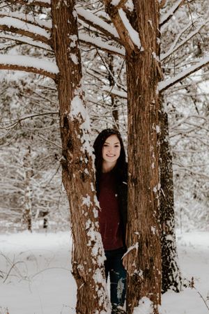Person standing between snow-covered trees in winter forest setting.