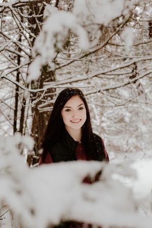 Artistic winter portrait through snow-covered branches in forest.