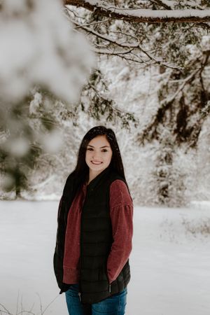 Person in red sweater and black vest standing in snowy winter landscape.
