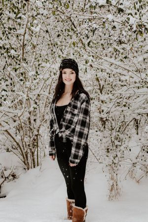 Winter portrait of person in plaid shirt and beanie standing amid snow-covered branches.