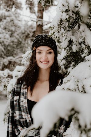 Close-up winter portrait of person in plaid and beanie next to snowy branches.