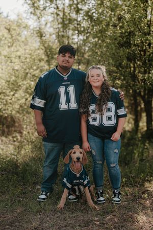 A family in sports jerseys posing with their dog wearing matching team gear.